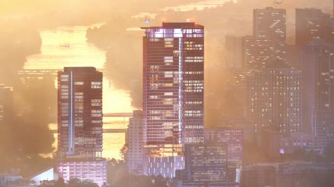 Rendering of two high-rise buildings, one taller than the other, in front of a river that recedes in golden twilight in the background. There is a group of taller buildings in the mist on the right. There appear to be helicopters landing on top of both of the foregrounded buildings.