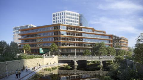Rendering of a five-story office building with horizontal bands of floor-to-ceiling windows and overhangs on every floor. In front is a somewhat sentimentalized creek and older concrete bridge with a new, multilevel pedestrian walkway to the left. The top of a taller, rectangular building is behind it.