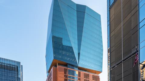 Photo of a tall new building with a metal-clad parking podium and glass-clad floors on top.