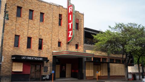 A three story brick building and former theater built in the 1920s. There is a blade-type sign in front that reads "Ritx."