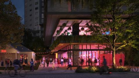 Rendering of the bottom two floors of a contemporary building, primarily glass, at twilight. The interior of the building is lighted. On the sidewalks and plazas in front and on the side, people are sitting on plater walls and walking around. On the left side, there's a small, refurbished old bungalow with people sitting at tables in front.