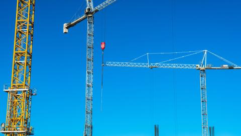 Photo of three construction cranes at different angles in front of an empty sky.