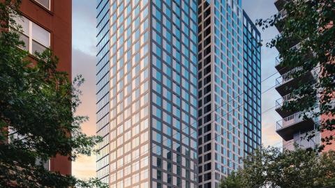 Vertical photo of a new glass 30-story building with slightly shorter buildings on each side.