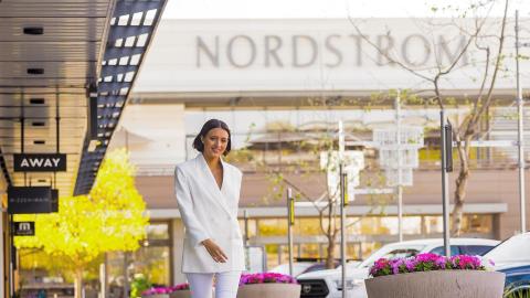 Stock image of an open air mall with a woman in a white pantsuit walking away from a Nordstrom.