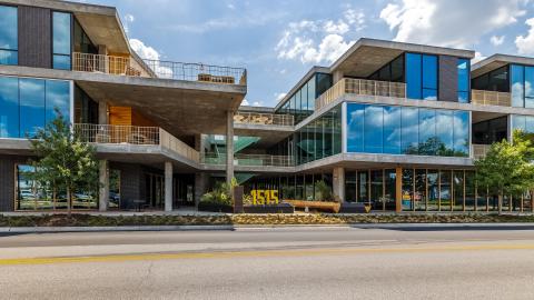 Rendering of a three-story contemporary building with staggered floors, a center courtyard and walkways open to the street, and mirrored windows.