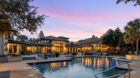 Photo of a vaguely Italianate, two-story apartment building entrance with a pool in front at dusk.