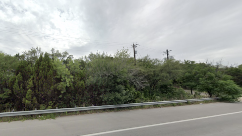 Screenshot of a wooded area with a couple of telephone poles behind a guard rail and a lane of highway.