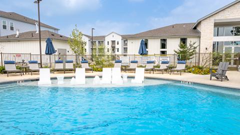 Photo of a large, new apartment complex with several four-story building and a prominently featured pool with fountains.