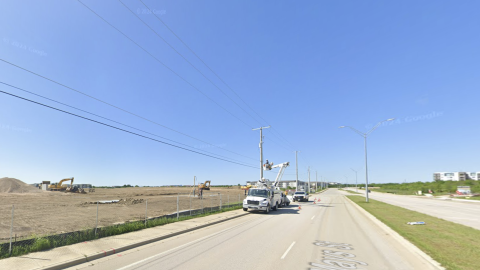 Screenshot of a photo of a highway with a construction site being bulldozed on one side and some apartments on the other side.